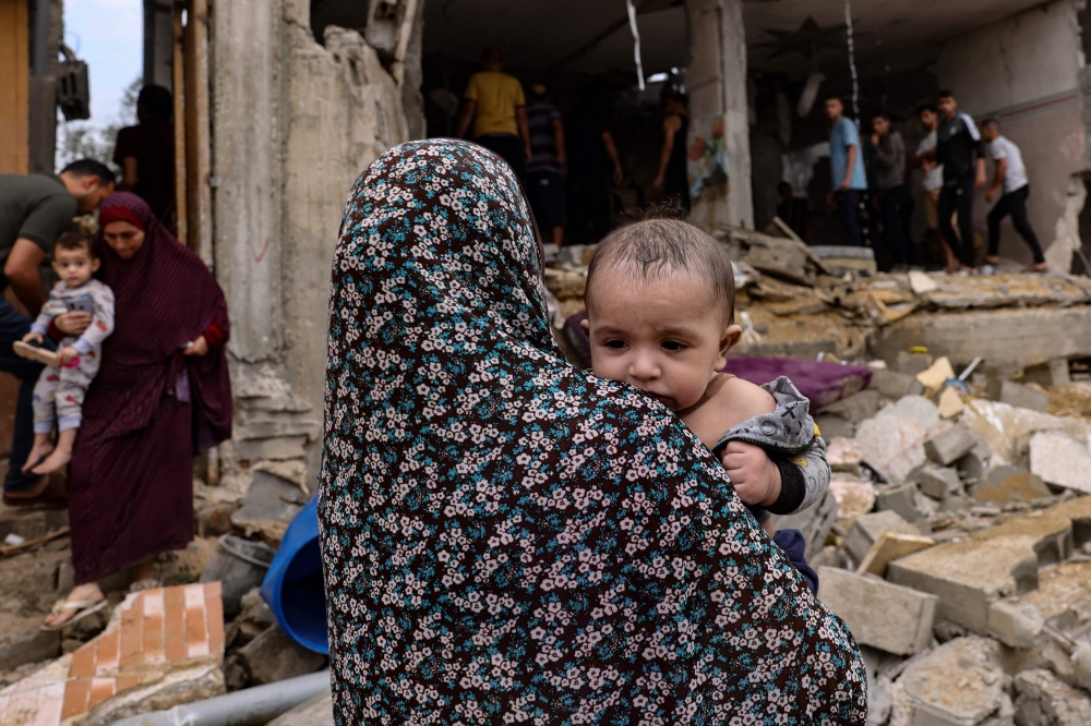 Women carry children as others check the damage in the aftermath of Israeli bombing in Rafah in the southern Gaza. — AFP 