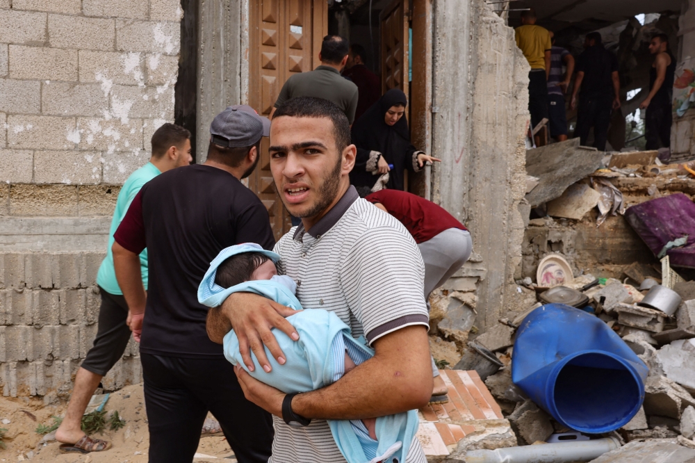 A man carries a baby as others check the damage in the aftermath of Israeli bombing in Rafah in the southern Gaza Strip on October 29, 2023