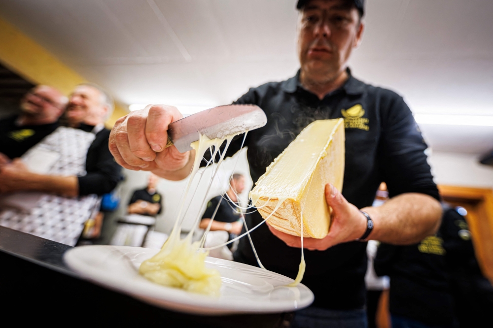 TOPSHOT - A "scaper" prepares a raclette during the first-ever Raclette World Championships featuring local and international raclette cheeses, in Morgins, on October 28, 2023. Up in the Swiss Alps, the air hangs thick with the funk of hot cheese as the planet's best melt away the competition at the inaugural Raclette World Championships. The Swiss native dish dates back centuries to a time when mountain herdsmen would heat their cheese on an open fire and scrape off the melted part to keep them going. (Photo by VALENTIN FLAURAUD / AFP)

