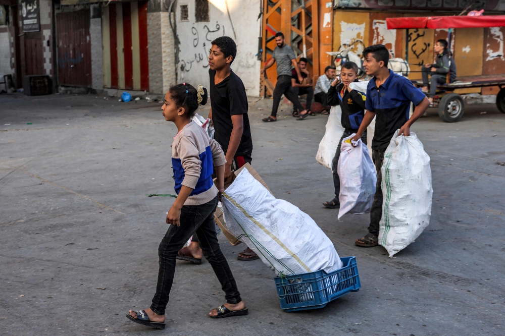 Youths walk with sacks filled with cardboard pieces to be used for fire-making along a street in Rafah in the southern Gaza Strip. — AFP 