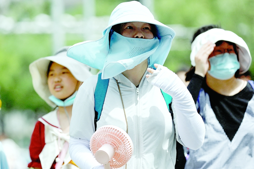 People wearing sun protection gear amid a heatwave walk on a street in Beijing. — Reuters