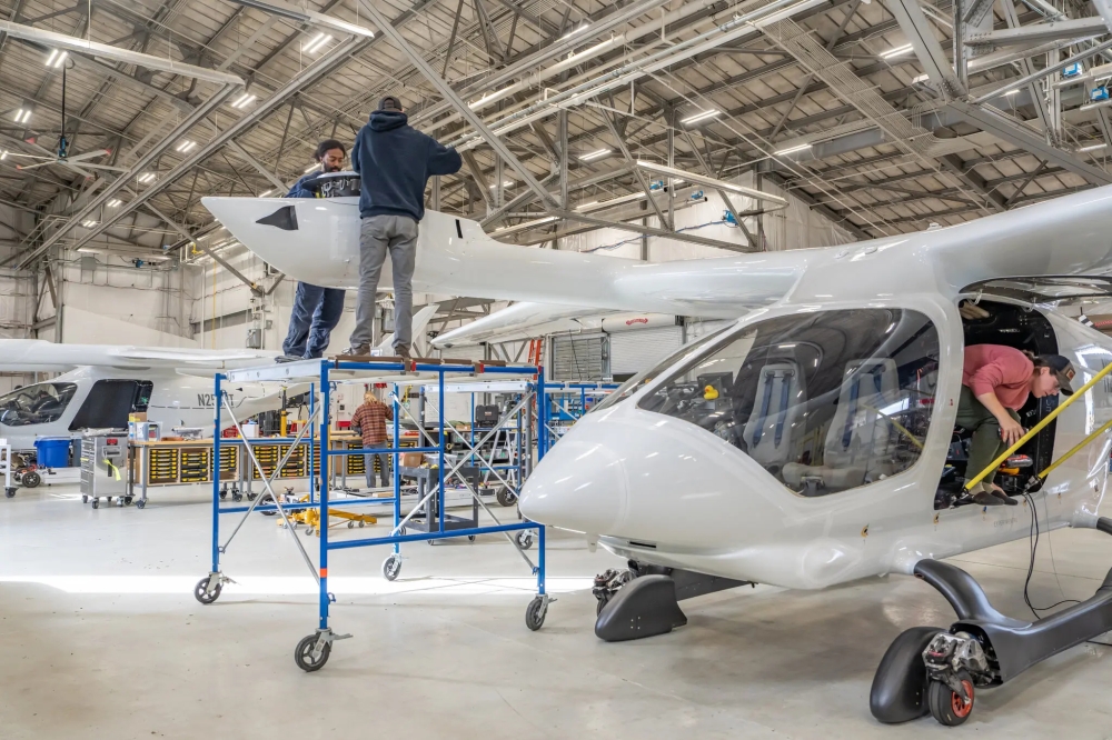 Beta Technologies employees working on two electric planes, one takes off like a conventional plane and the other takes off and lands like a helicopter.
