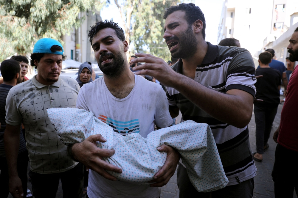 A Palestinian holds the body of a child wrapped in a shroud as another reacts next to him, outside a hospital following Israel's bombardment of Gaza City's eastern suburb of Shujaiya. - AFP