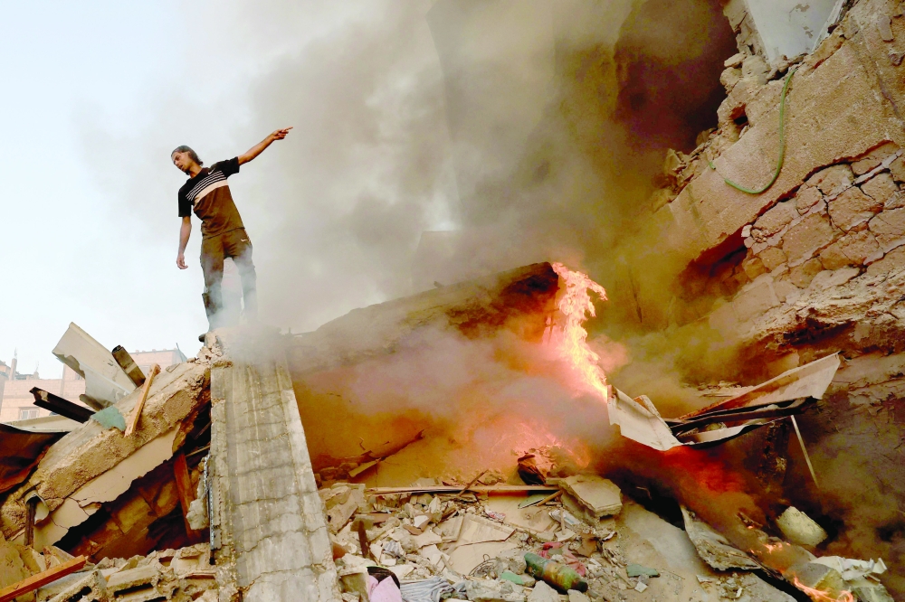 A Palestinian man gestures as he stands on the rubble of a collapsed building on Khan Yunis. — AFP
