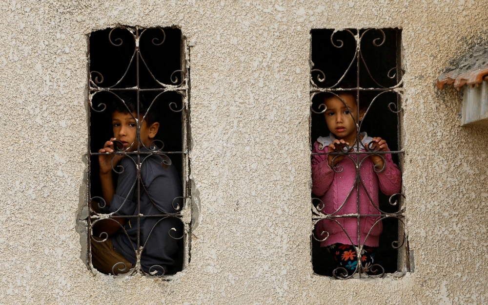 Palestinian children look out from a window with a grill at the site of Israeli strikes on houses, amid the ongoing conflict in Khan Younis in the southern Gaza Strip. - Reuters
