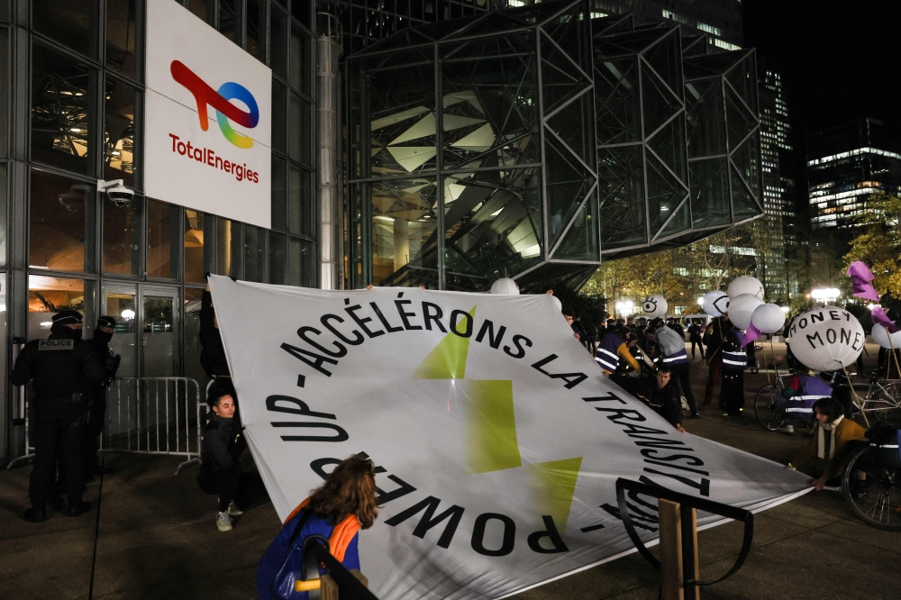 Demonstrators display a "Power Up -Accelerate the transition" banner as they prepare an illuminated "Tax'N Roll" parade from La Defense to Place Vauban, as part of a "Power Up" action of 350.org asking for a "just ecological transition, taking into account the historical responsibilities of major polluters" ahead of the international climate conference COP28, in front of the TotalEnergies headquarter building at La Defense, in Courbevoie on November 3, 2023. (Photo by Alain JOCARD / AFP)