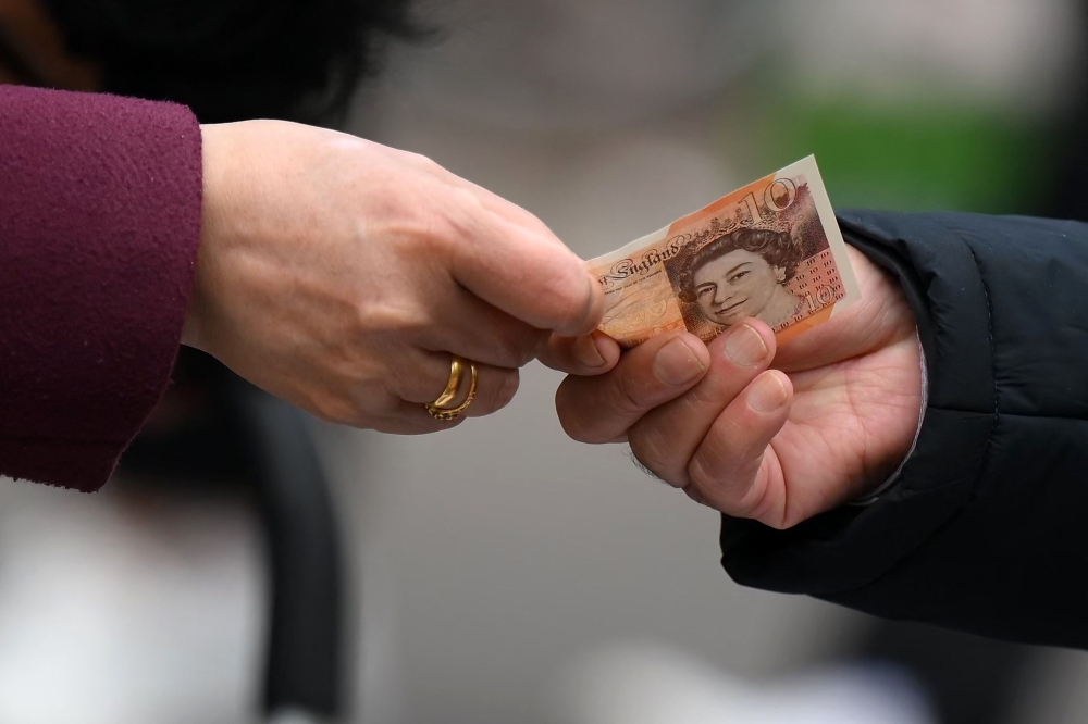A customer uses a ten pound note to pay for goods at a market in east London. - AFP File