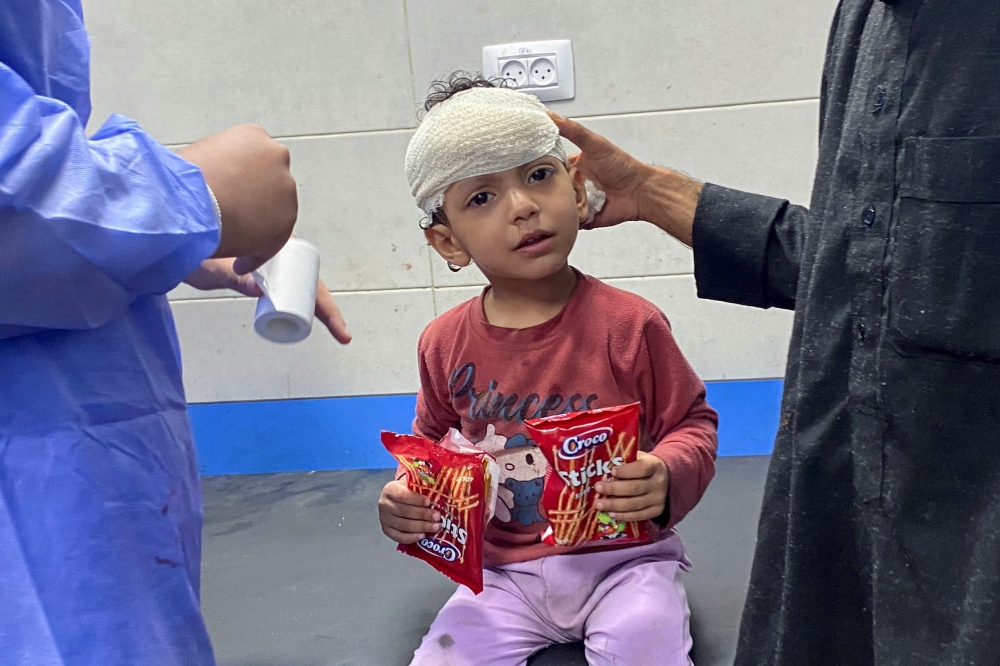 Palestinian girl Orheen Al Dayah, who was injured on her forehead in an Israeli strike is assisted after she had her wounds stitched without anaesthesia, at Al Shifa hospital in Gaza City. - Reuters