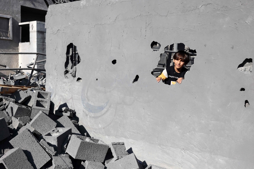 A child peeks through a hole in the wall of a building destroyed in an Israeli strike on Rafah in the southern Gaza Strip on Friday. — AFP