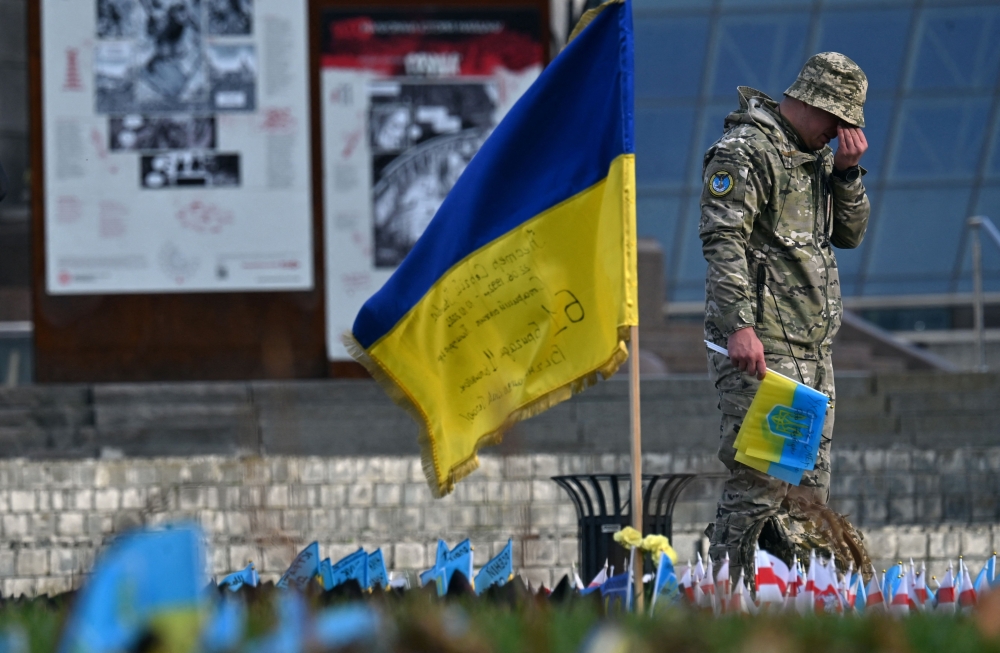 A serviceman mourns next to a Ukrainian flag at a makeshift memorial for fallen soldiers at Independence Square in Kyiv amid the Russian invasion of Ukraine. - AFP



