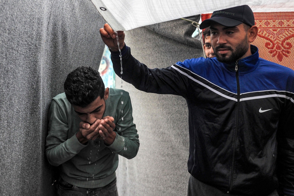 Men use their hands to drink rainwater dripping from the roof of a tent amid water shortages at a school run by the United Nations Relief and Works Agency for Palestine Refugees in the Near East in Rafah. - AFP

