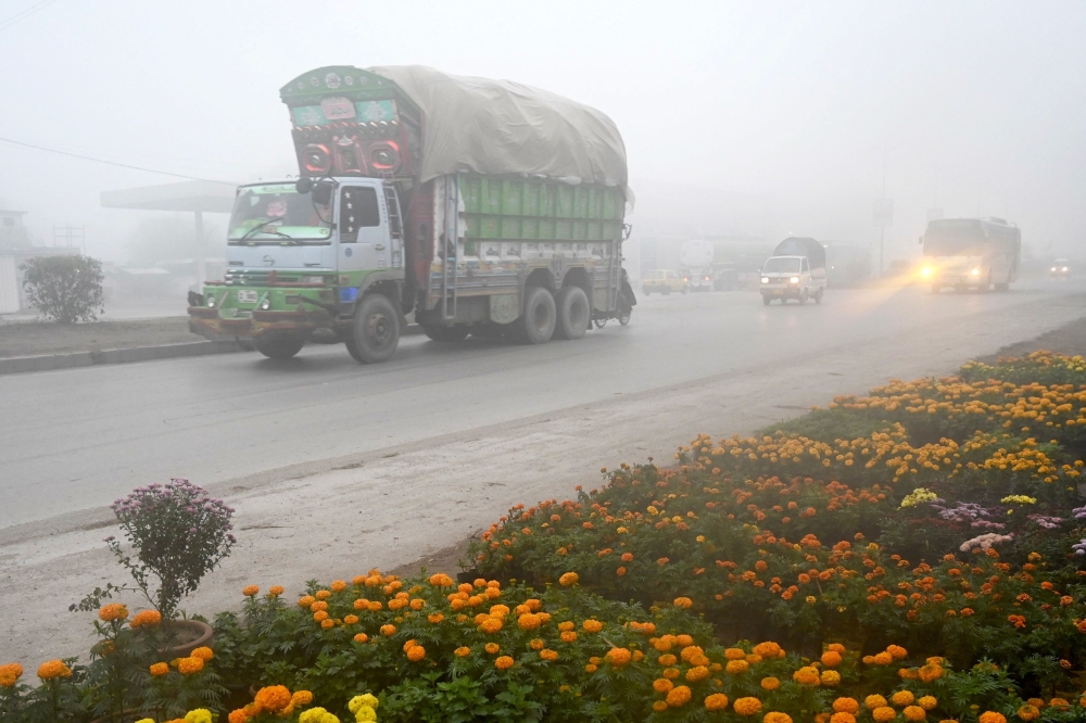 Vehicles ride along a street  amid foggy conditions in Peshawar