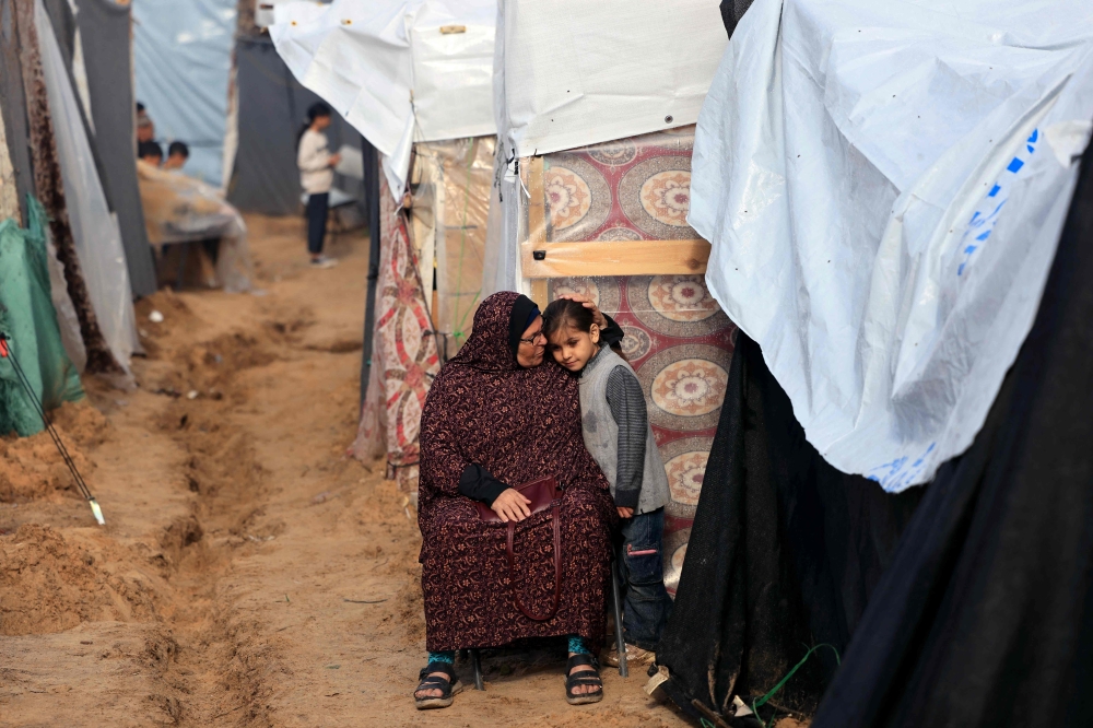 A displaced Palestinian girl, cuddles up to an older woman as they sit outside a makeshift shelter after overnight rainstorms in Khan Yunis. — AFP 