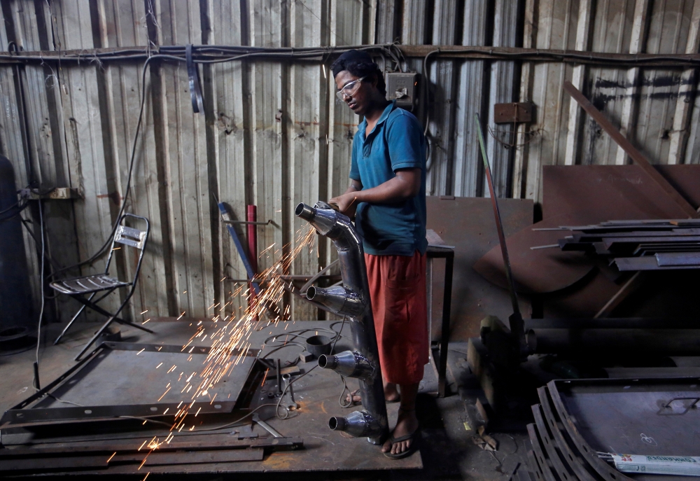 A worker grinds a steel pipe to be used in air ducts inside a workshop at an industrial area in Mumbai