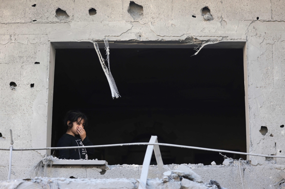 A Palestinian girl looks out of a window of a damaged building at the Nuseirat refugee camp in the central Gaza Strip on Friday. - AFP