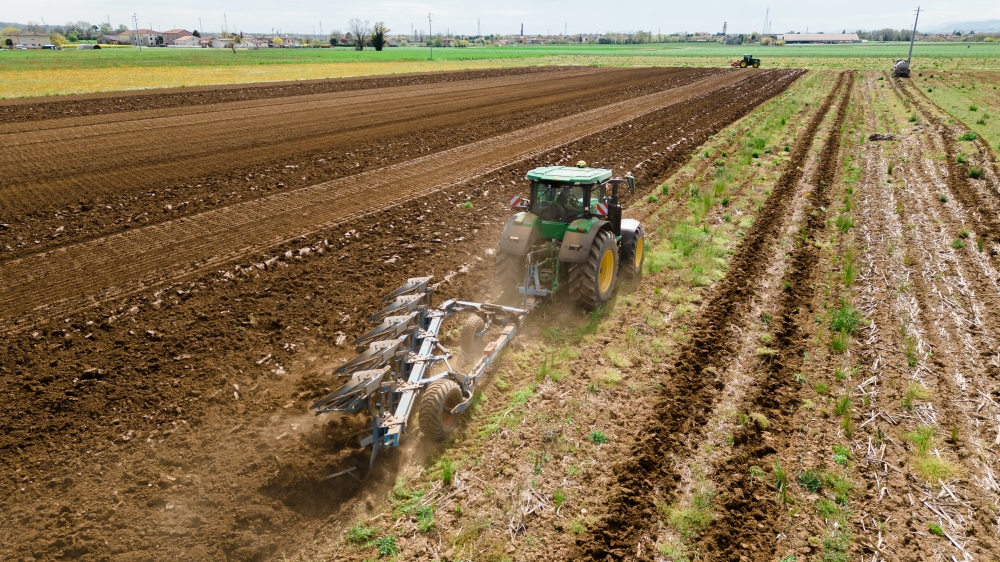 A photograph of a rural landscape with a farmer using a tractor to prepare the soil for crop rotation, showcasing the use of farming machinery and equipment. The image highlights the importance of field management and soil preparation in achieving higher agricultural profitability.
