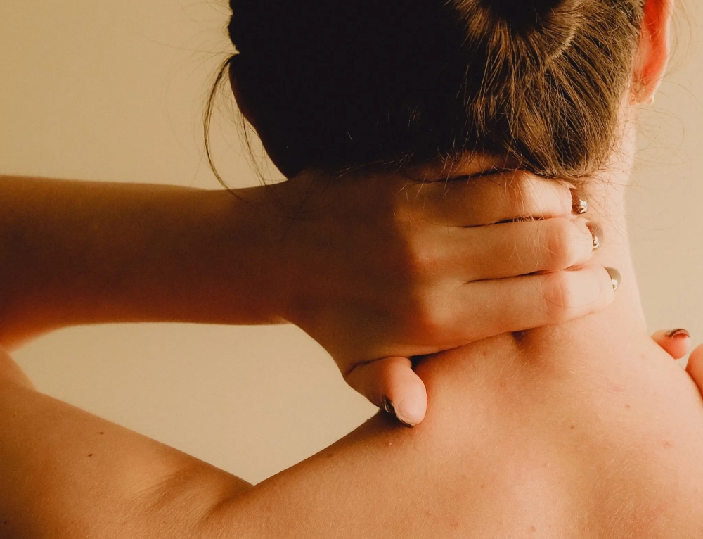 Portrait of young woman massaging her painful neck over grey