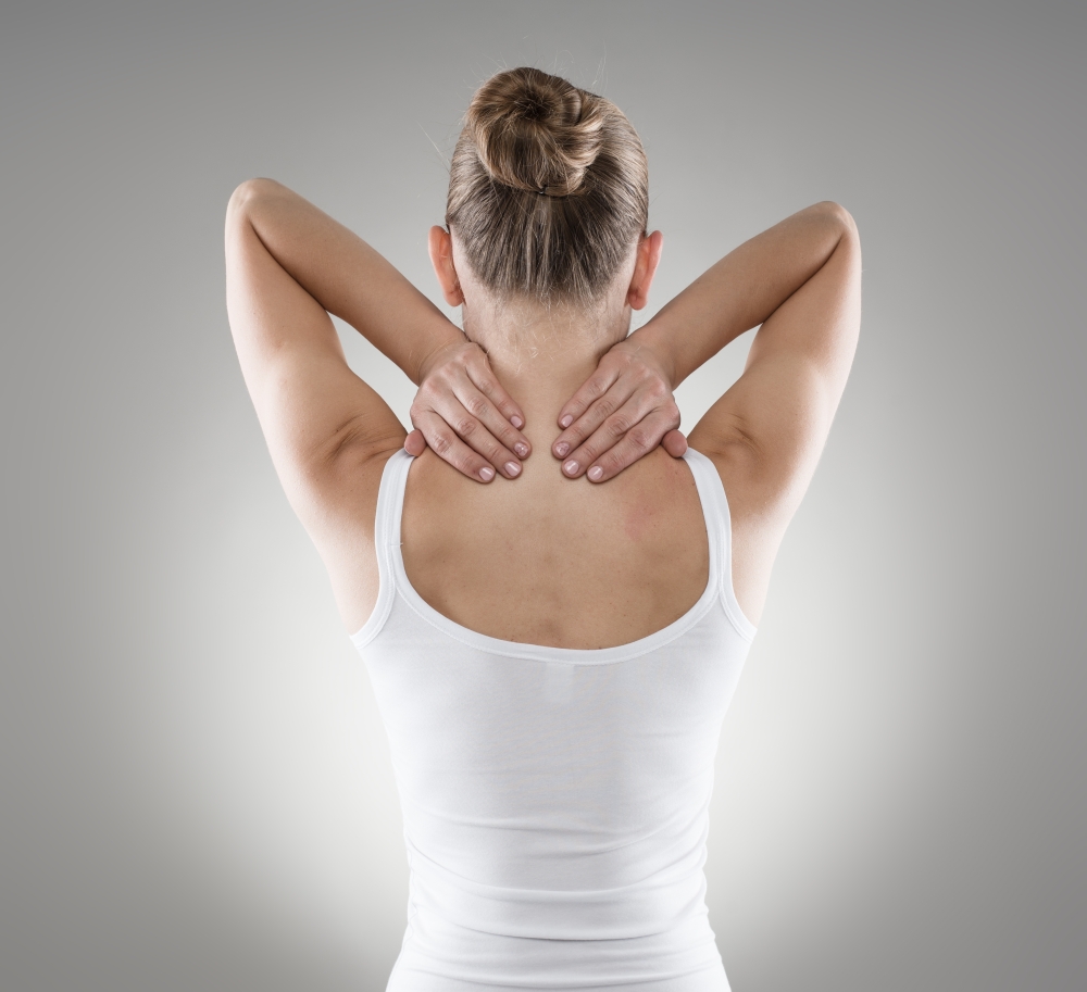 Portrait of young woman massaging her painful neck over grey