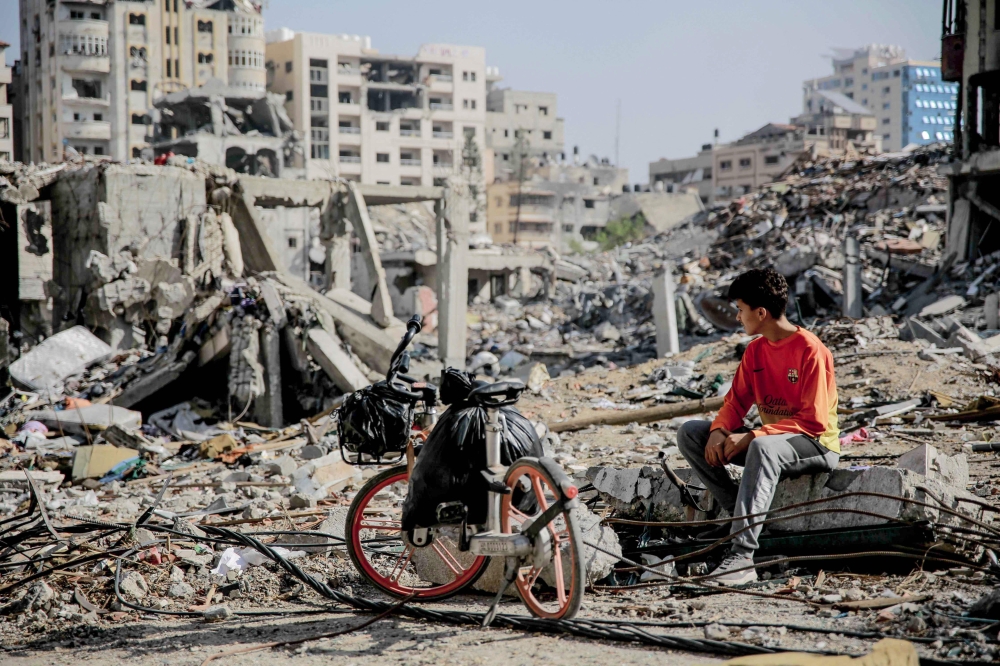 A Palestinian youth sits next to his bicycle amid the rubble of destroyed buildings in Gaza City on the northern Gaza strip. — AFP 