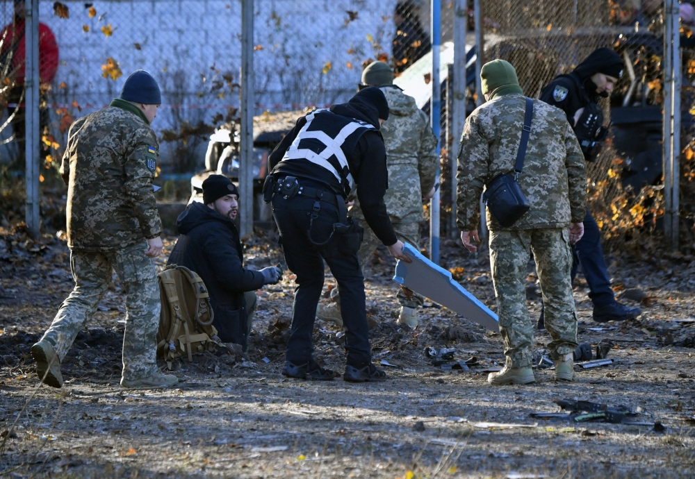 Ukrainian police and military experts collect fragments of downed Russian drone around a crater in a yard amid residential buildings in Kyiv. — AFP 