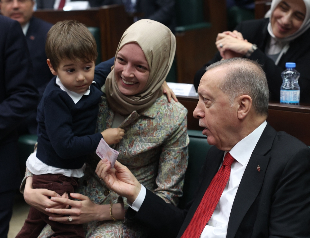 Turkish President and AK Party Chairman Recep Tayyip Erdogan gives money to the son of AK Party MP Zehra Nur Aydemir during his party's group meeting at the Turkish Grand National Assembly in Ankara on Wednesday. — AFP 