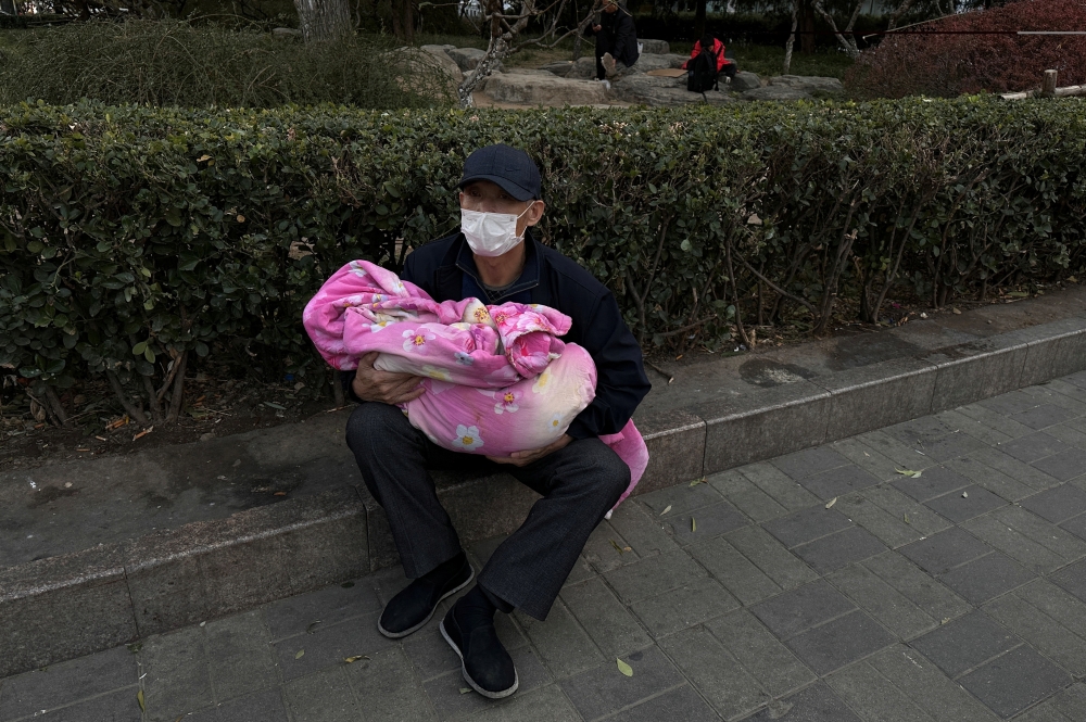 Man carrying a child sits outside a children's hospital in Beijing. — Reuters