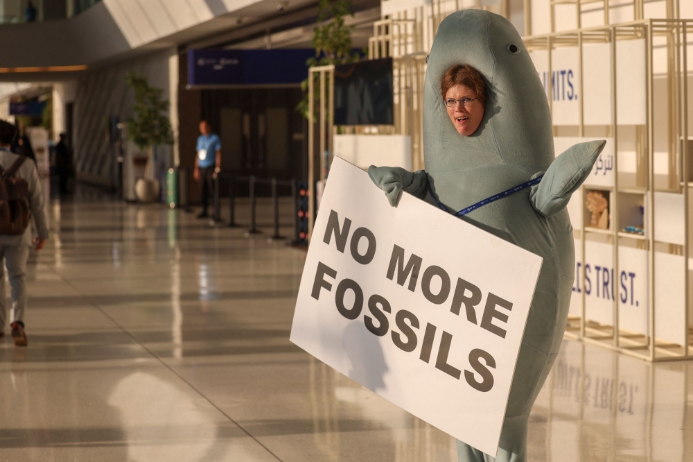An environmental activist wearing a costume displays a placard in a hallway during the COP28 United Nations climate summit in Dubai on December 3, 2023.  