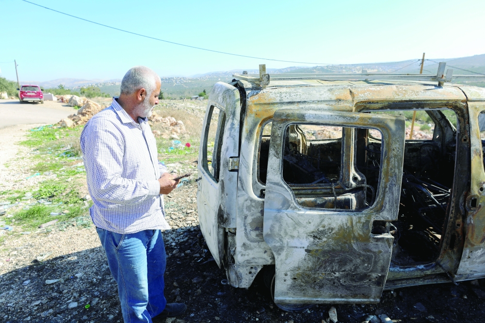 A Palestinian checks a car burned in Israeli settlers raid near Salfit in the West Bank. — Reuters 