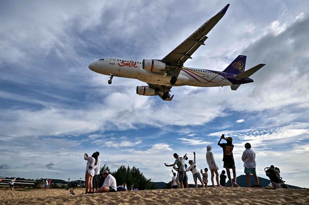 Tourists posing for pictures on the Mai Khao Beach as an airplane lands at Phuket International Airport 