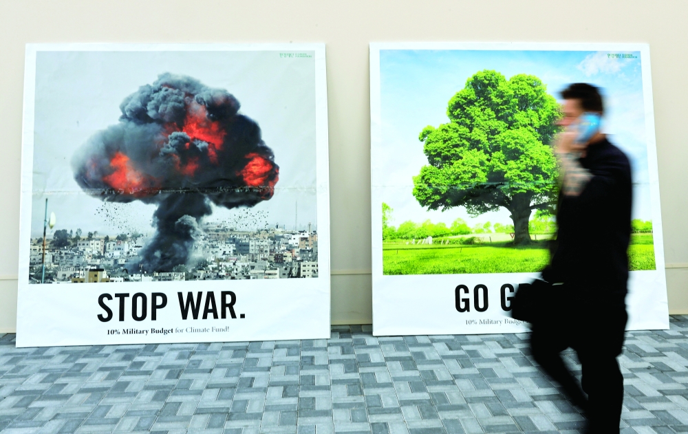 A man walks past a wall with two banners that read 'Stop war' and 'Go green' at the United Nations Climate Change Conference (COP28) in Dubai, UAE. - Reuters 
