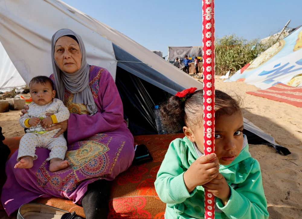 A woman holds a baby next to a girl, as displaced Palestinians shelter in a tent camp near the border with Egypt