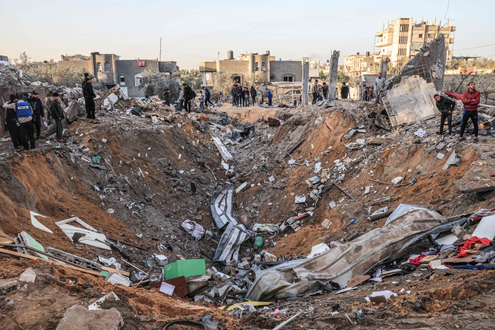 TOPSHOT - People search building rubble for items to salvage following an early morning Israeli strike in Rafah in the southern Gaza Strip on December 12, 2023, amid ongoing battles between Israel and the Palestinian militant group Hamas. (Photo by SAID KHATIB / AFP)

