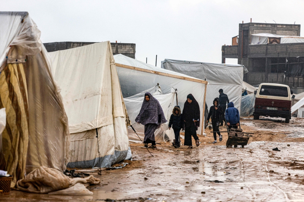 Palestinians walk under the rain at a camp for displaced people in Rafah, in the southern Gaza Strip. — AFP 