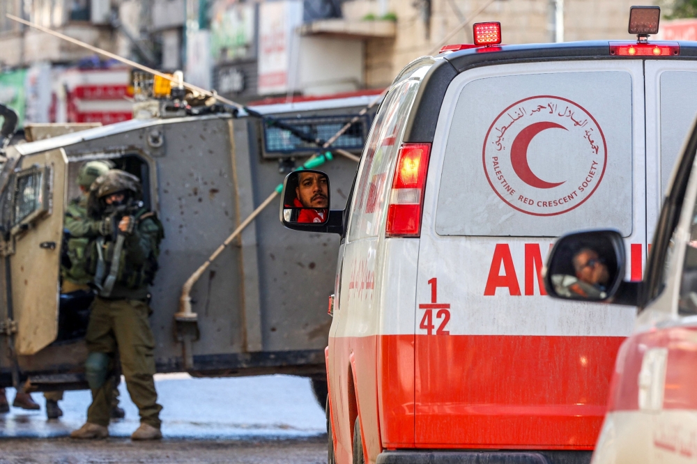 An Israeli soldier aims his weapon as Palestinian Red Crescent ambulances wait. — AFP 