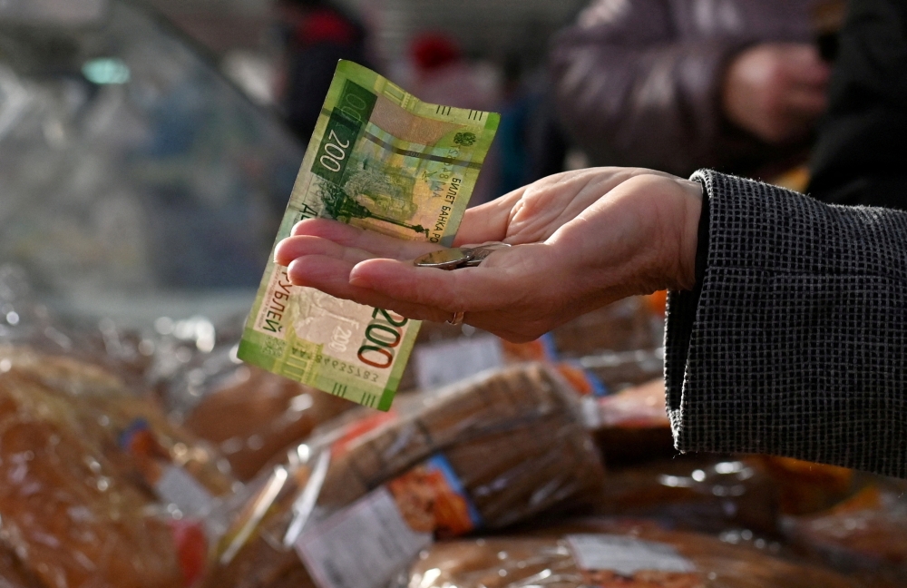 A customer hands over Russian rouble banknotes and coins to a vendor at a market in Omsk, Russia. — Reuters