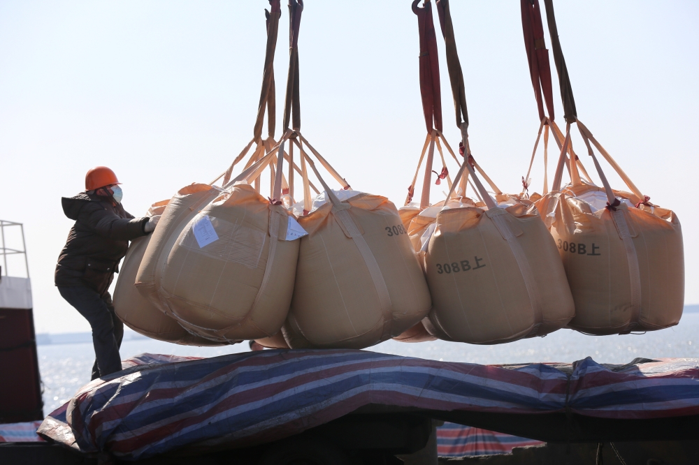 Worker wearing a face mask transports fertilisers for export at a port in Nantong, China. — Reuters