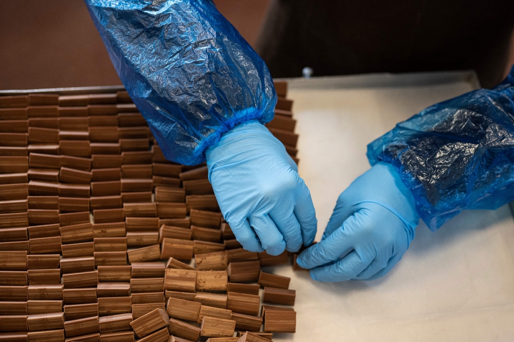 An employee prepares a tray of the famous chocolate treat shaped like lingots, the 'Gianduiotto' at Guido Castagna laboratory, on December 12, 2023 in Giaveno near Turin, Northwestern Italy.  In Turin, a committee was formed made up of large and small local chocolate producers in order to obtain PGI recognition (Protected Geographical Indication) for one of the most famous products in the area: the gianduiotto. But the Swiss Lindt group, owner of the Caffarel brand, opposes it. (Photo by MARCO BERTORELLO / AFP)

