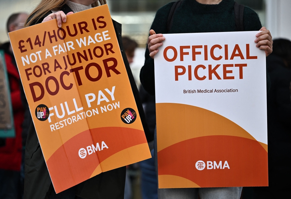 People hold British Medical Association branded placards calling for better pay, as they stand on a picket line outside University College Hospital in central London during a strike by junior doctors -- physicians who are not senior specialists but who may still years of experience. - AFP File