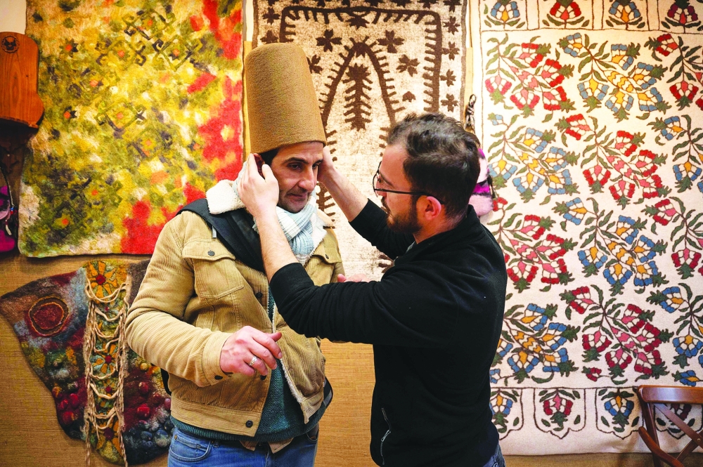 Yunus Girgic adjusts as he delivers a symbolic hat 'Sikke', worn by whirling dervishes, to his customer Ashmi Benmehidi (L), a French musician who left an insurance job in Montpellier, South of France, to practice the art of the ney, in a workshop in Konya. - AFP