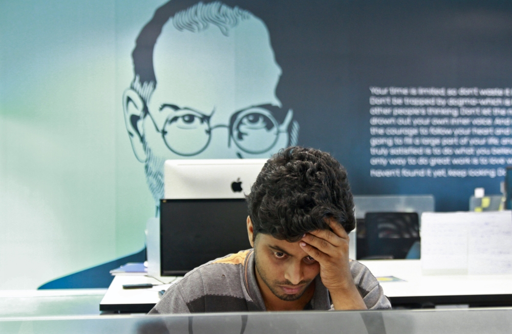 An employee works on a computer terminal against the backdrop of a picture of late Apple co-founder Jobs at the Start-up Village in Kinfra High Tech Park in Kochi, India. — Reuters