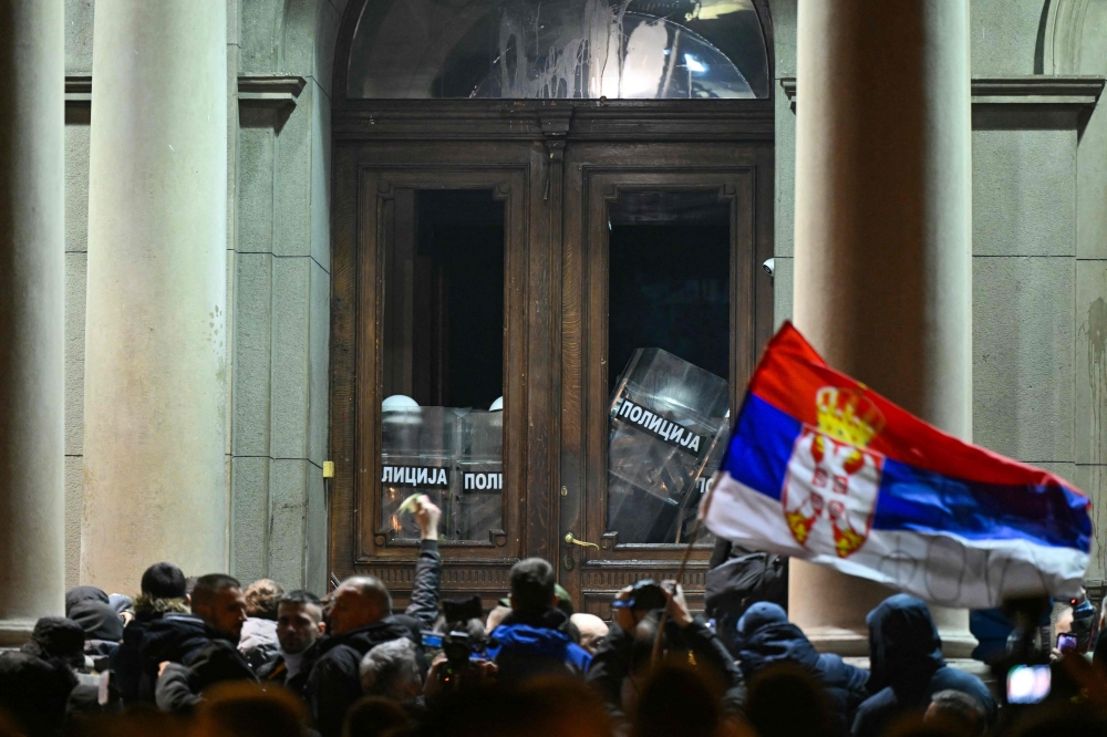 Opposition supporters gather in front of Belgrade's city council building as police officers stand behind the city council's doors during a protest in Belgrade. — AFP 