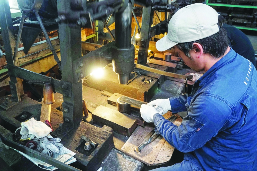 This photo taken on November 15, 2023 shows knife maker Yoshihiro Yauji placing a "santoku", a multipurpose knife, under a spring hammer at the Takefu Knife Village in the town of Echizen, Fukui prefecture. Blacksmith Yoshihiro Yauji pulls a piece of glowing metal from the forge in a Japanese village, continuing a tradition dating back centuries to when the region was renowned for crafting swords carried by samurai. - TO GO WITH Japan-culture-knives,FOCUS by Saad SAYEED