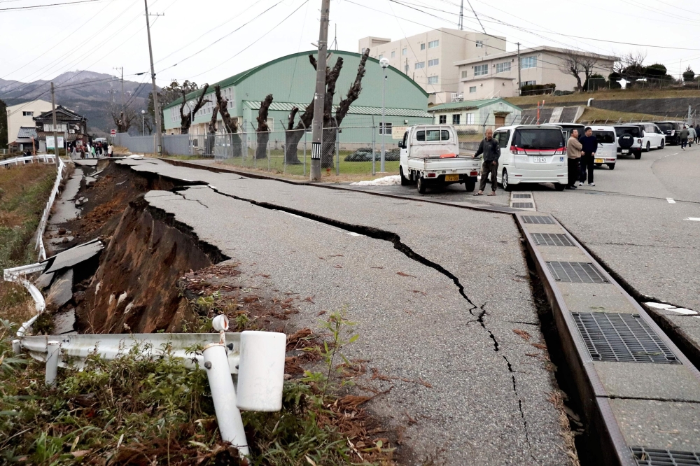 People stand next to large cracks in the pavement after evacuating into a street in the city of Wajima, Ishikawa prefecture. — AFP 