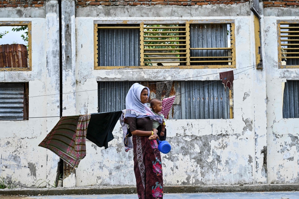 A Rohingya refugee carries her child as she stands at a temporary shelter at a government building in Banda Aceh. — AFP file photo