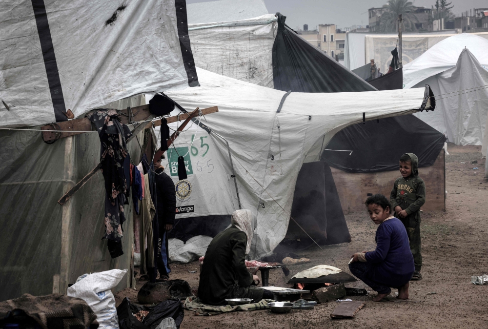 A Palestinian woman makes bread outside a tent at a makeshift camp housing displaced Palestinians, in Rafah. — AFP 