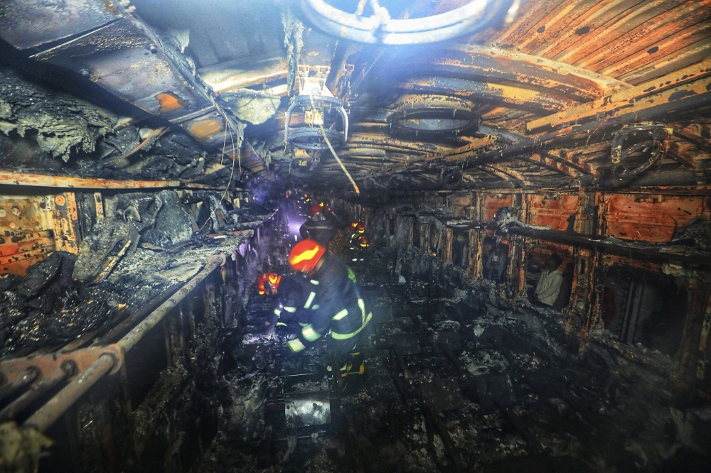 Fire fighters search through a burnt-out carriage of the Benapole Express in Dhaka on January 5