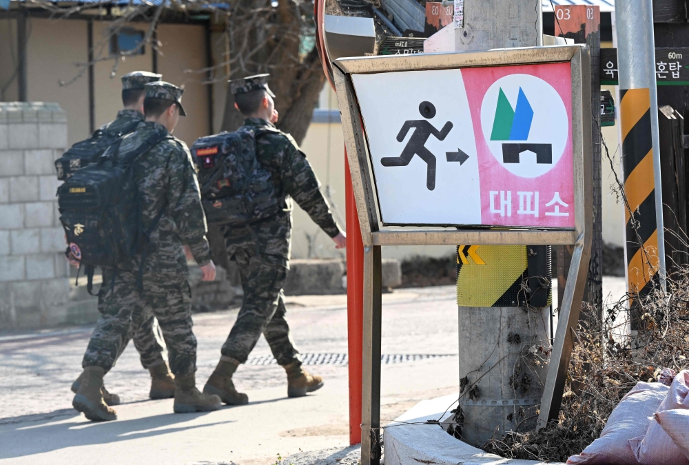 South Korean marines walk past a shelter sign in a village of Yeonpyeong island, near the 'northern limit line' sea boundary with North Korea. — AFP 