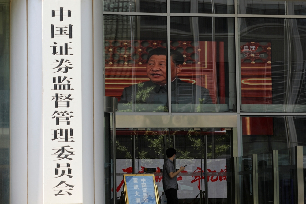 A man stands near a screen showing news footage of Chinese President Xi Jinping at the China Securities Regulatory Commission (CSRC) building on the Financial Street in Beijing. — Reuters