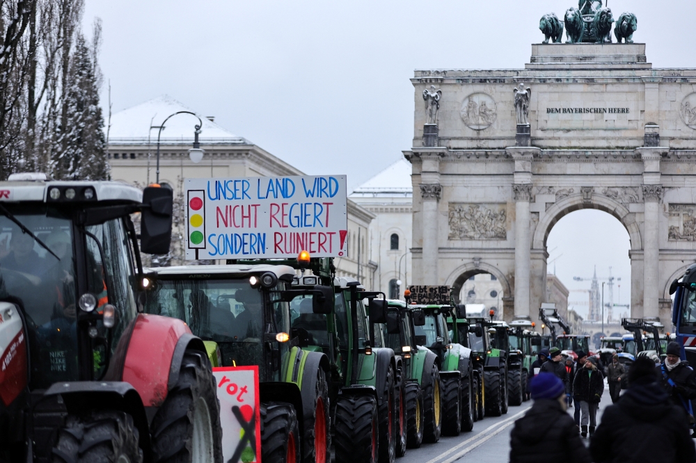 People walk near farm vehicles, as German farmers take part in a protest against the cut of vehicle tax subsidies, near the Victory Gate 'Siegestor', in Munich. — Reuters 