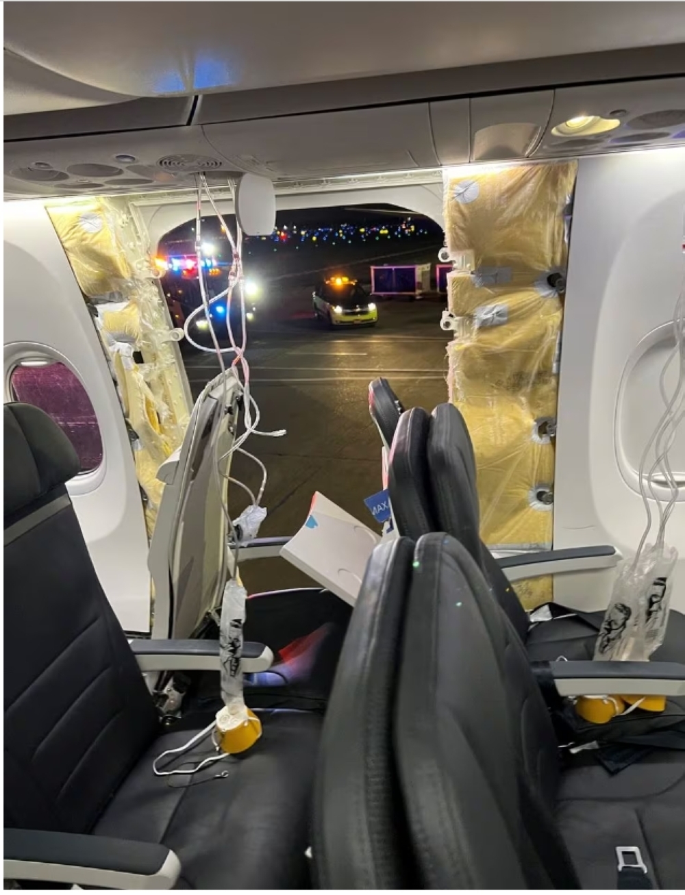 Passenger oxygen masks hang from the roof next to a missing window and a portion of a side wall of an Alaska Airlines Flight 1282
